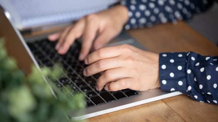 A student types a college essay on a laptop at a wooden desk