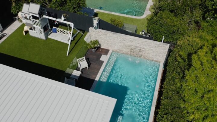 Aerial view of a compact backyard pool beside a patio and small lawn area