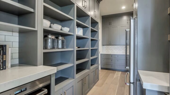 Compact butler pantry with gray open shelves, marble counters, recessed lights, and a stainless fridge