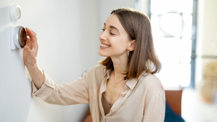 A woman adjusts a smart thermostat on a white wall