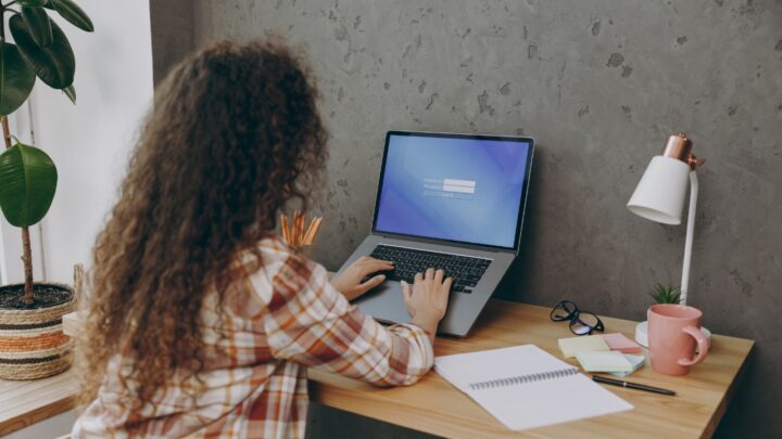 A woman enters a login on a laptop at a home desk