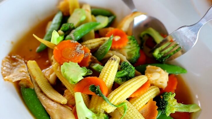 Mixed vegetables with baby corn, carrots, broccoli, and snap peas sit in a white bowl