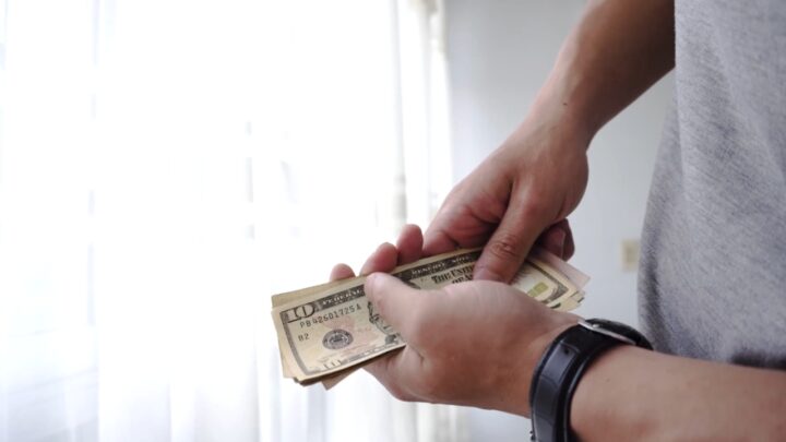 A person counts dollar bills near a bright window