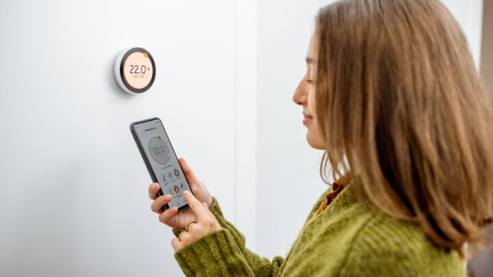 A woman controls a smart thermostat with a phone