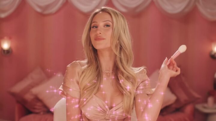 Alix Earle holds a makeup brush in a pink bedroom