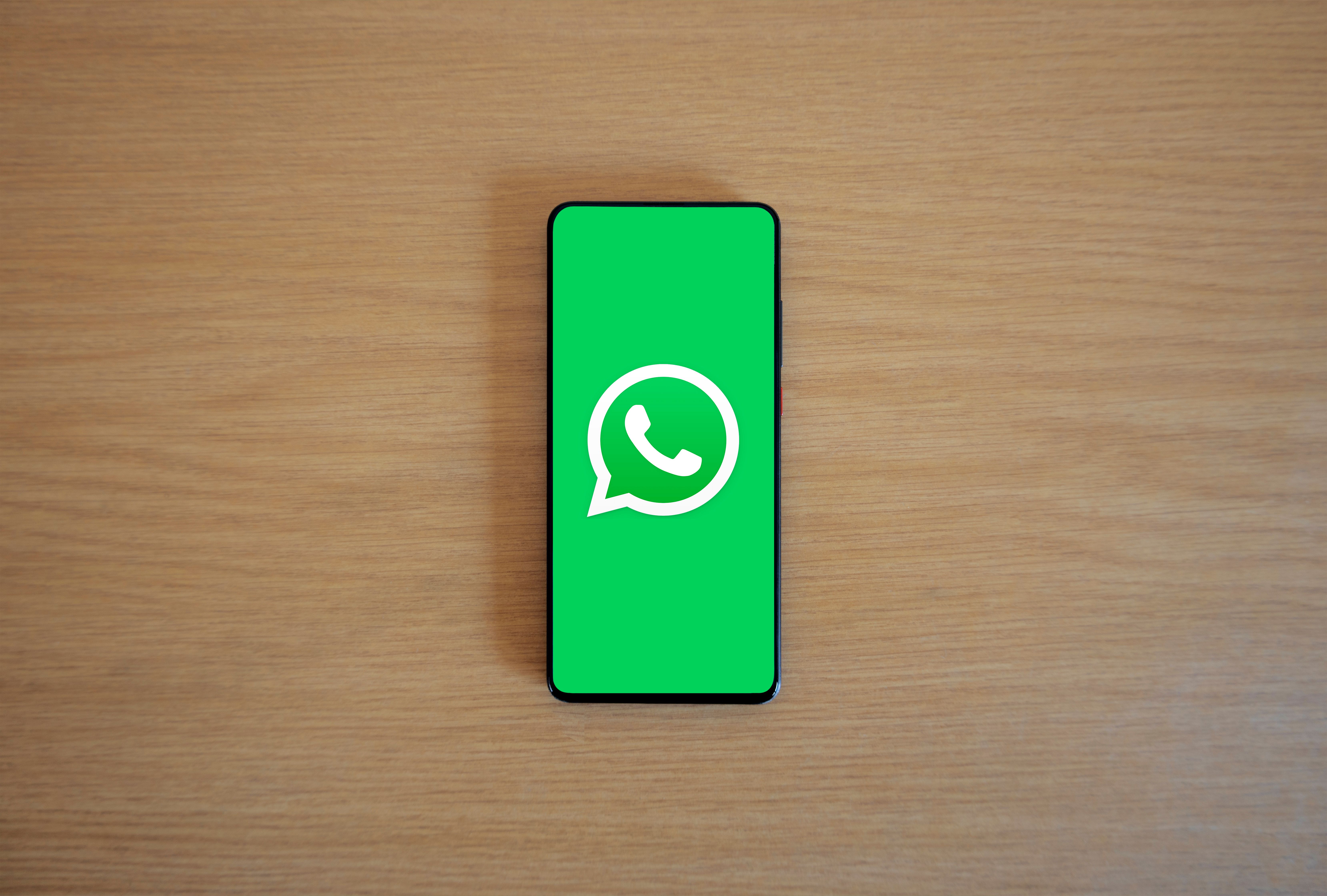 Top view of a smartphone showing the WhatsApp logo on a wooden surface
