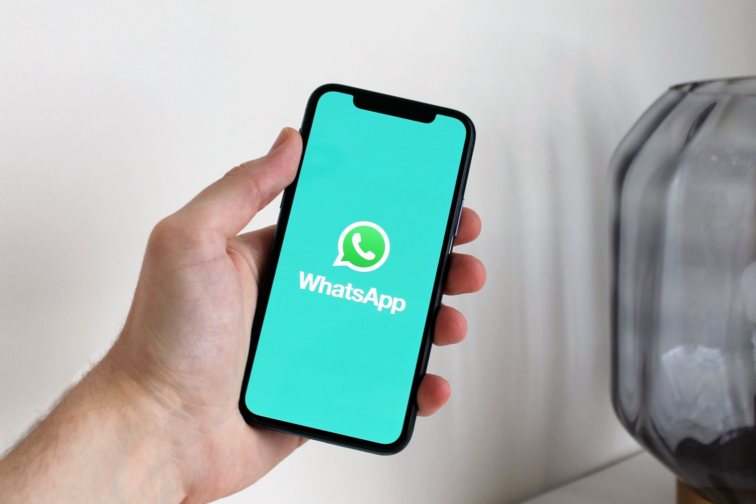 Hand holding a smartphone displaying the WhatsApp messaging app, illustrating encrypted messaging for business customer contact